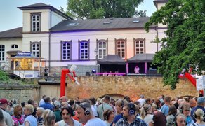 Silent Disco im Schlosspark Peine: Viele Besucher mit Funkkopfhörern feiern vor der historischen Schlosskulisse, während DJs auf der Brücke für Stimmung sorgen.