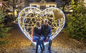 Paar sitzt in einer beleuchteten Herz-Lichtskulptur auf der Weihnachtsstadt in der Innenstadt von Peine, umgeben von geschmückten Tannen und warmem Lichterglanz am Abend.