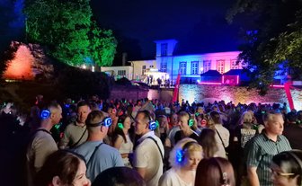 Große Menschenmenge mit leuchtenden Kopfhörern bei einer Open-Air-Party vor einem beleuchteten Gebäude in der Nacht.