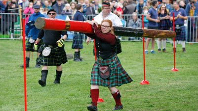 Teilnehmerin im Kilt läuft mit Baumstamm bei Highland Games im Peiner Stadtpark vor Publikum durch einen Slalom