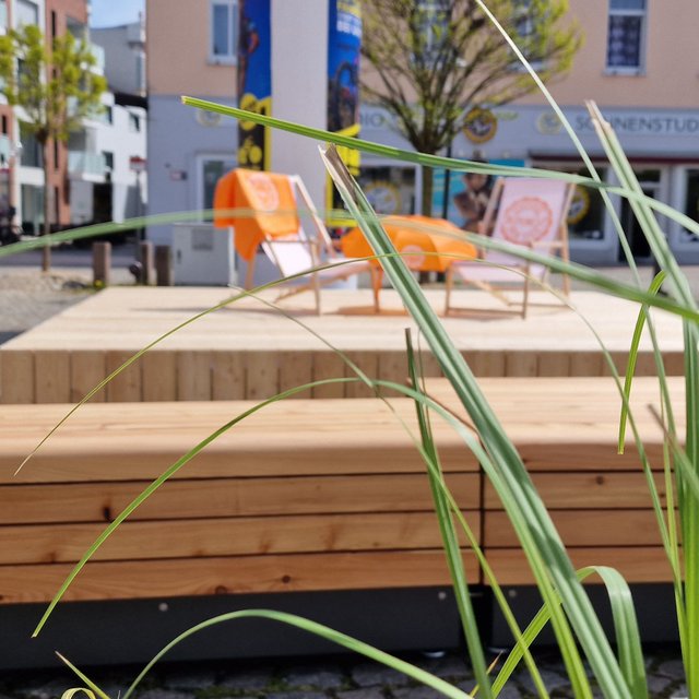 Open Stage in der Peiner Innenstadt mit Holzplattform, Sitzgelegenheiten und Begrünung als offener Treffpunkt für Kultur, Begegnung und urbanes Stadtleben.