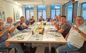 Eine Gruppe von Menschen an einem Tisch blickt in die Kamera und hebt die Gläser.