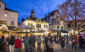 Weihnachtsmarkt mit zahlreichen Besuchern vor historischen Fachwerkhäusern und beleuchteten Ständen bei Abenddämmerung.