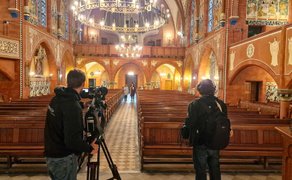 Zwei Männer filmen zwei Frauen, die den Gang eines Kirschenschiffs entlanggehen.