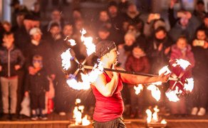 Feuerkünstler bei einer Feuershow vor Publikum, mit brennenden Fackeln in beiden Händen.