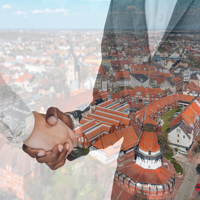 Zwei Personen geben sich die Hand; darübergelegt ist eine Luftaufnahme der Peiner Innenstadt mit roten Dächern und dem historischen Mühlenturm als Symbol für Partnerschaft und Zusammenarbeit.