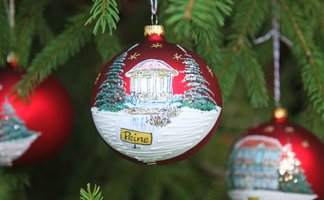 Rote Christbaumkugel mit winterlicher Landschaft und Schriftzug 'Peine' hängt an Tannenzweig neben einer einfarbigen roten Kugel.