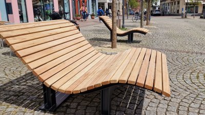 Geschwungene Sonnenliegen aus Holz und Stahl als moderne Stadtmöblierung im urbanen Stadtraum der Peiner Innenstadt, die zum Verweilen und Entspannen einladen.