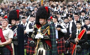 Gruppe von Menschen in traditioneller schottischer Kleidung mit Kilts und Hüten bei einer Veranstaltung im Freien.