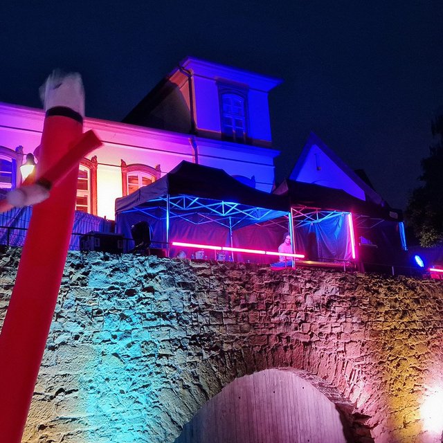 Open-Air-Event im Peiner Burgpark bei Nacht: farbig illuminierte historische Fassade, DJ unter beleuchtetem Zelt, tanzende Besucher und rote LED-Lichtinstallationen bei der Silent Music Party in Peine.