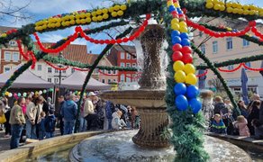 Festlich geschmückter Osterbrunnen auf dem Marktplatz in Peine mit bunten Girlanden, Ballons und vielen Besuchern.