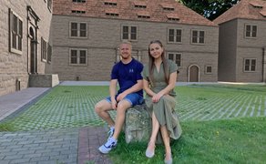 Zwei Personen sitzen im Außenbereich vor einer mittels Augmented Reality dargestellten historischen Burganlage und sind Teil einer digitalen Rekonstruktion der Peiner Burg.