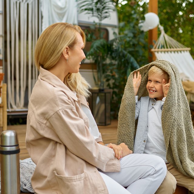 Das Bild zeigt eine Mutter mit ihrem Sohn, die vor einem Campingwagen sitzen und Spaß haben. 