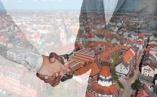 Zwei Personen geben sich die Hand; darübergelegt ist eine Luftaufnahme der Peiner Innenstadt mit roten Dächern und dem historischen Mühlenturm als Symbol für Partnerschaft und Zusammenarbeit.