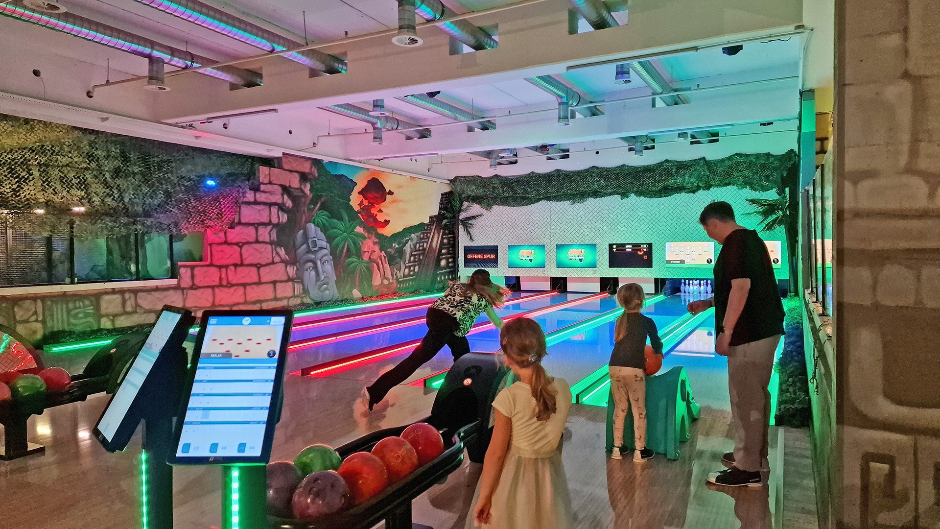 Das Bild zeigt Menschen, die auf einer Bowlingbahn spielen.