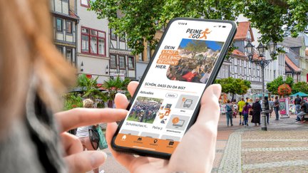 Das Bild zeigt eine Frau, die ein Handy in der Hand hält, auf dem die City App Peine2Go zu sehen ist.