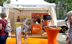 Besucher stehen vor dem Informationsstand der Peine Marketing GmbH mit Prospekten und Ausstellungsmaterial.