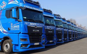 Reihe blauer Sattelzugmaschinen der Marke MAN mit Aufschrift „FRITZ BENTE SPEDITION“ und „SPEZIALTRANSPORTE“ auf der Front, geparkt auf einem Hof.