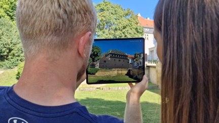 Zwei Personen nutzen Augmented Reality auf einem Tablet, um historische Gebäude in Peine digital zu entdecken, vor Ort in einer Grünanlage.