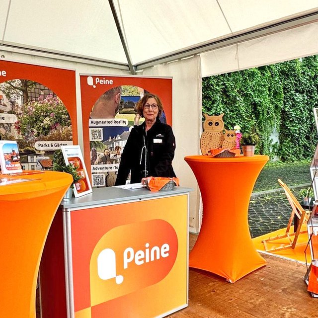 Messestand von Peine Marketing beim Entdeckertag mit orangefarbenen Infoständen, Informationsmaterialien und zwei Mitarbeiterinnen.