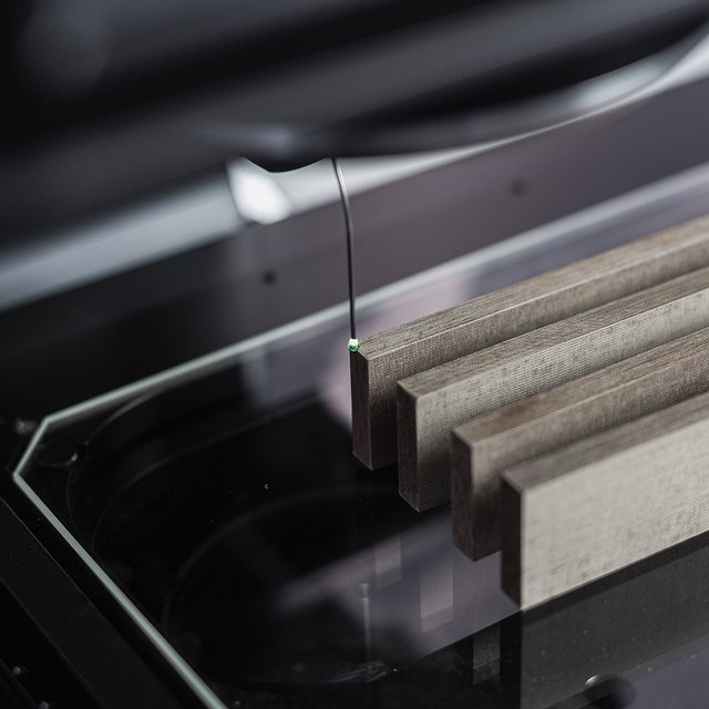 Messmaschine mit drei rechteckigen grauen Proben auf einer Glasplatte unter einem Messsensor.