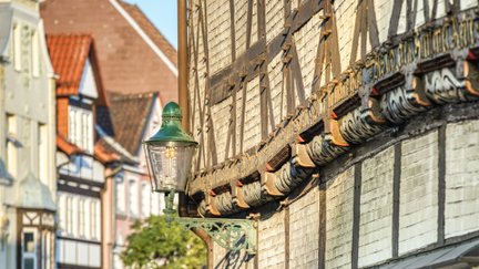 Historische Fachwerkfassade in der Peiner Innenstadt mit dekorativer Straßenlaterne und traditionellen Bauelementen im Sonnenlicht.