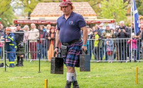 Teilnehmer im Kilt trägt schwere Gewichte beim Highland Game „Farmer’s Walk“ vor Publikum im Peiner Stadtpark