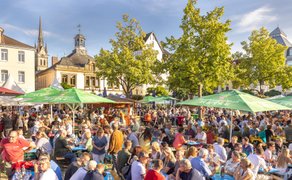 Belebtes Peiner Weinfest auf dem Marktplatz mit vielen Besuchern an Biertischen, grünen Sonnenschirmen und historischer Altstadtkulisse bei sonnigem Wetter.
