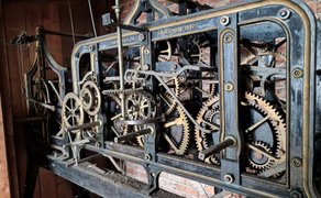 Ein mechanisches Uhrwerk mit vielen Zahnrädern ist im Turm der St.-Jakobi-Kirche Peine vor einer Ziegelwand zu sehen.