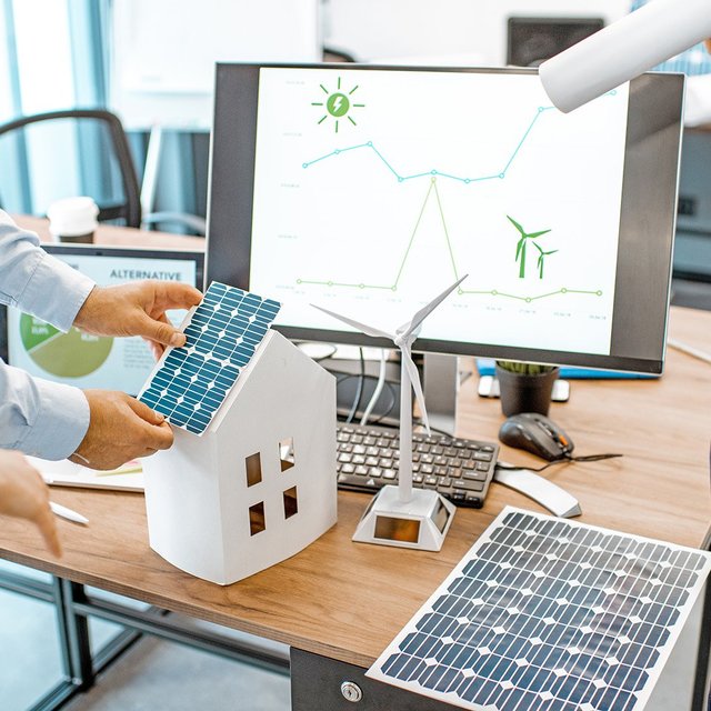 Personen arbeiten am Modell eines Hauses mit Photovoltaikmodulen.