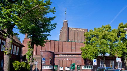 Historische Außenansicht der Härke-Brauerei Peine mit markantem Backsteinbau und dem Schriftzug „Härke-Bier“ am Turm. Die traditionsreiche Braumanufaktur ist von Bäumen eingerahmt und steht sinnbildlich für Biergenuss und Braukultur aus Peine.