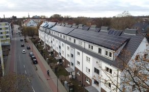 Reihenhaus mit Solarpaneelen auf dem Dach an einer Straße mit parkenden Autos und Bäumen im Herbst.