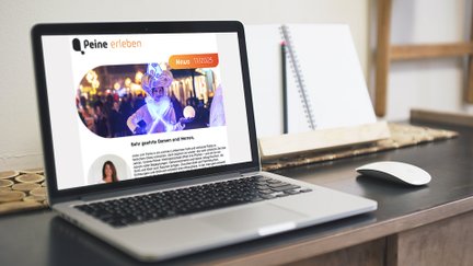 Laptop auf Holztisch zeigt Newsletter mit Foto einer Person in Kostüm vor Weihnachtsbeleuchtung.