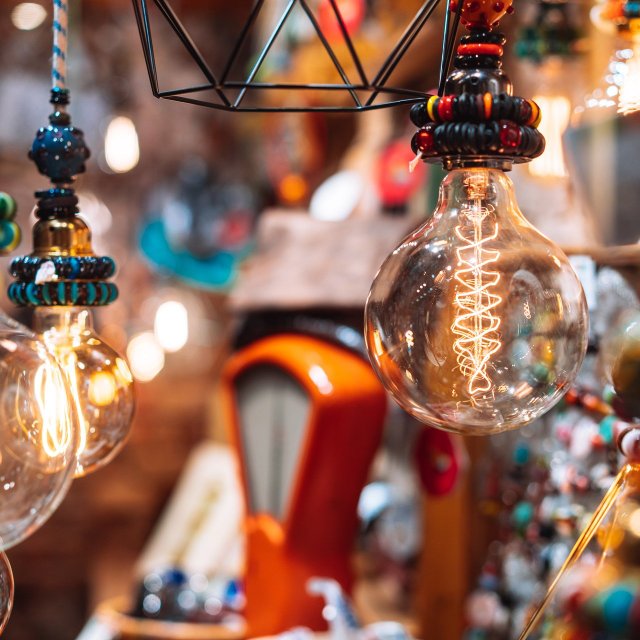 Detailaufnahme von kunsthandwerklichen Lampen mit dekorativen Glühbirnen: Handgefertigte Leuchten aus Glas, Metall und bunten Perlen leuchten warm und schaffen eine gemütliche Atmosphäre auf einem Kunsthandwerkermarkt in Peine.