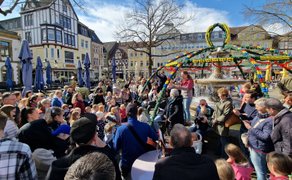 Viele Besucher feiern den Osterbrunnen auf dem Marktplatz in Peine mit Musik, Familien und frühlingshafter Dekoration.