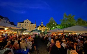 Peiner Weinfest am Abend mit dicht gedrängten Besucherinnen und Besuchern unter Sonnenschirmen, beleuchtetem Marktplatz, historischen Gebäuden im Hintergrund und stimmungsvoller Atmosphäre in der Innenstadt von Peine.