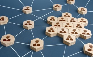 Holzplättchen mit stilisierten Personen in Anzügen, verbunden durch weiße Linien auf blauem Hintergrund, symbolisieren Netzwerk.