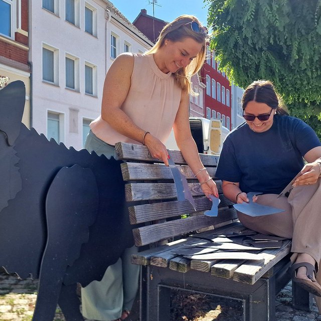 Peiner Projekte von der Initiative Stadtimpulse ausgezeichnet: Zwei Frauen puzzeln Metallteile an einer Bank mit Wolfsfigur.