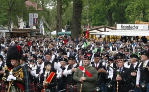 Große Parade von Dudelsackspielern in traditionellen schottischen Kilts beim Highland Gathering in Peine – zahlreiche Pipes-&-Drums-Bands marschieren durch den Park, begleitet von begeisterten Zuschauerinnen und Zuschauern.