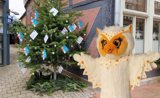 Uhlinchen steht neben einem geschmückten Weihnachtsbaum mit Wunschkarten in der weihnachtlichen Peiner Innenstadt.