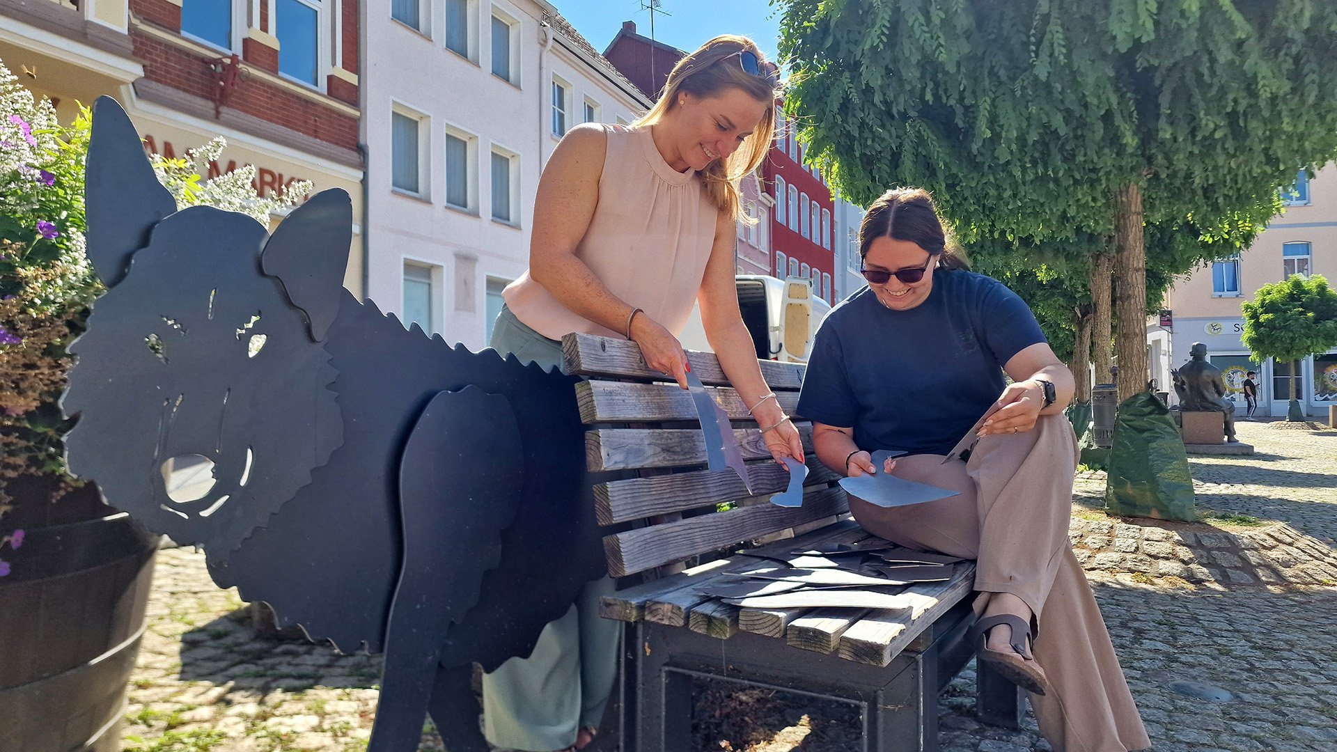 Peiner Projekte von der Initiative Stadtimpulse ausgezeichnet: Zwei Frauen puzzeln Metallteile an einer Bank mit Wolfsfigur.