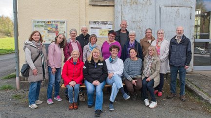 Gruppe von Menschen unterschiedlichen Alters vor einem Gebäude mit Informationsschildern an der Wand