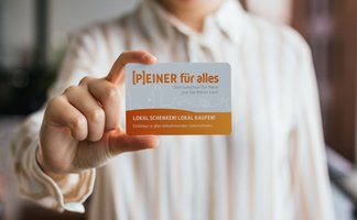 Eine Person hält den Gutschein „[P]EINER für alles“ in die Kamera – ein lokaler Geschenkgutschein für Peine und das Peiner Land.