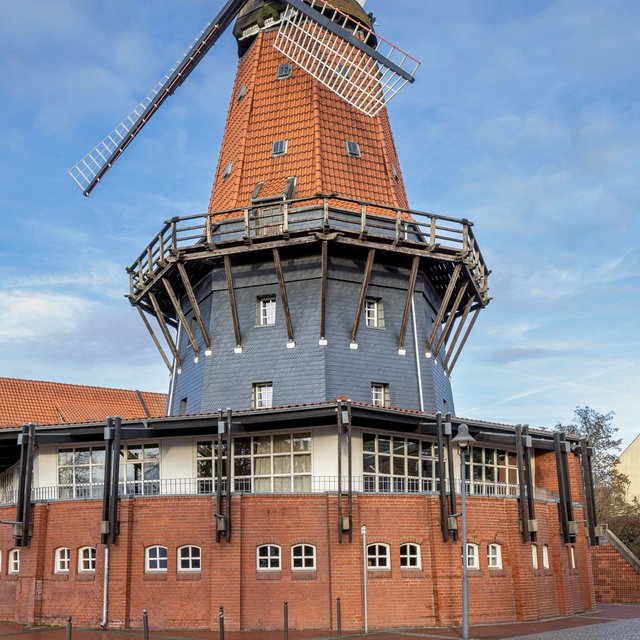 Historische Töpfers Mühle in Peine mit markantem Mühlenturm und Flügeln vor blauem Himmel.