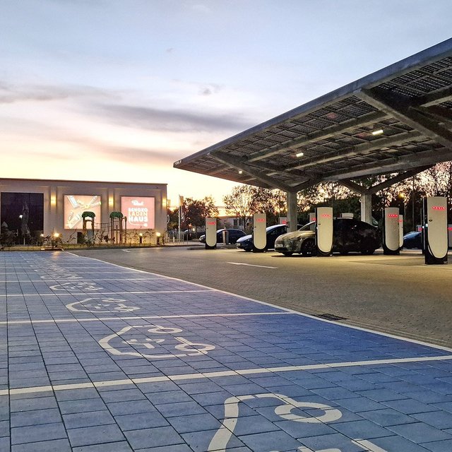 Das Bild zeigt eine Reihe von Parkplätzen mit Ladesäulen sowie ein Carport mit Solarzellen. 
