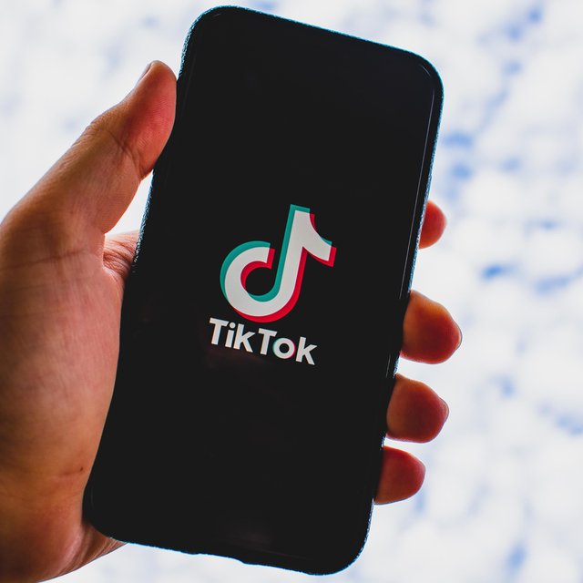 Das Bild zeigt eine Hand, die ein Handy hält, und auf dem das Logo der Plattform Tiktok zu sehen ist. 