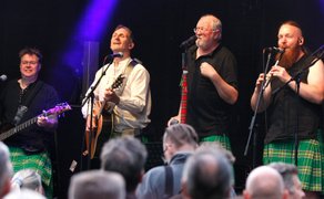 Band in Kilts spielt und singt schottische Folkmusik live auf der Bühne beim Highland Gathering vor Publikum