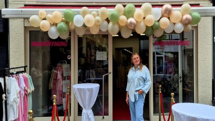 Neueröffnung eines Modegeschäfts in der Peiner Innenstadt mit Ballondekoration, rotem Teppich und Kleiderständern vor dem Eingang. Eine Frau steht lächelnd vor dem Laden.