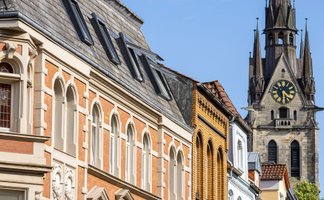 Das Bild zeigt eine historische Häuserzeile in der Peiner Innenstadt mit dem Kirchturm der St. Jakobi Kirche im Hintergrund. 