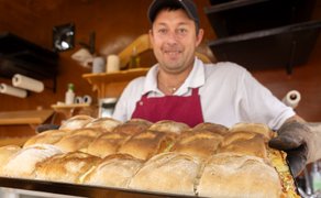 Ein Mann präsentiert ein Blech mit frisch gebackenem Handbrot in einem Verkaufsstand.